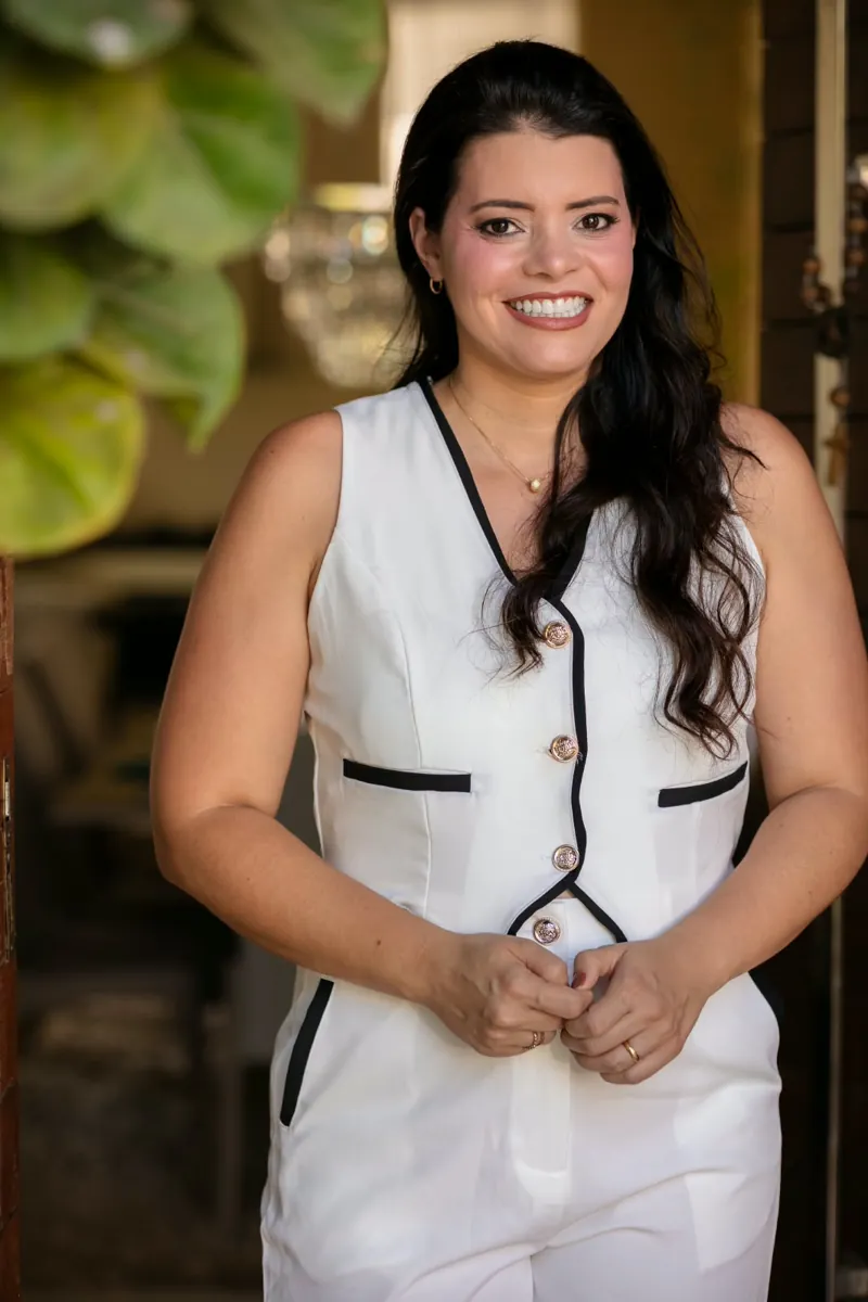 Angelina Freitas, fisioterapeuta, em pé, sorrindo, com as mãos unidas à frente